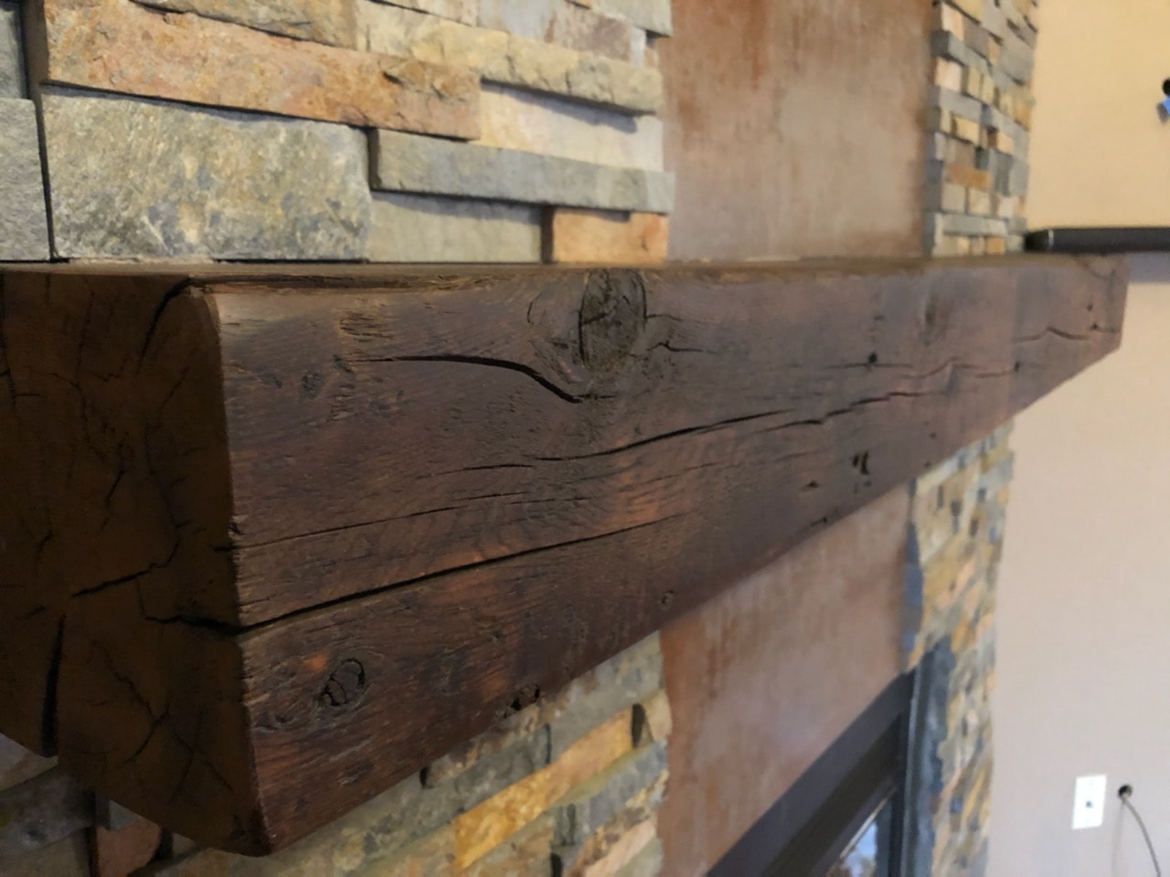 Norstone Ochre Stacked Stone Rock Panels on fireplace with a dark close up rustic wood mantle